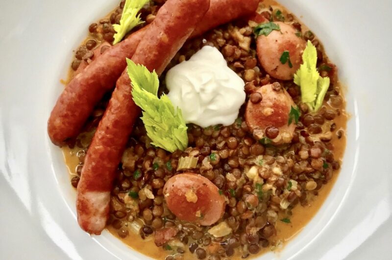 Soczewica gotowana z krojonymi warzywami doprawiona śmietaną i wzbogacona smażoną kiełbasą wędzoną w plastrach.