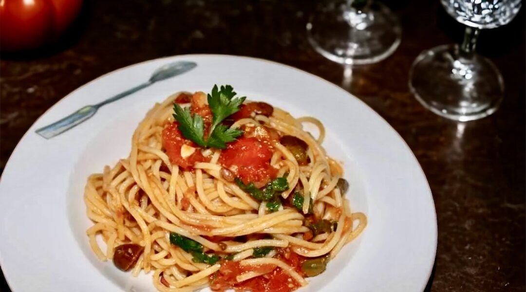 Makaron spaghetti podany z sosem alla Puttanesca przygotowanym na bazie kaparów, anchois, oliwek i pomidorów.