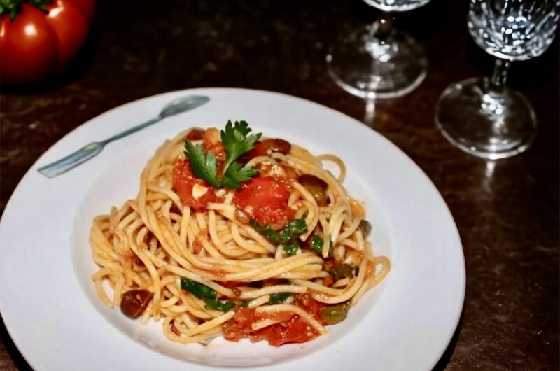 Makaron spaghetti podany z sosem alla Puttanesca przygotowanym na bazie kaparów, anchois, oliwek i pomidorów.