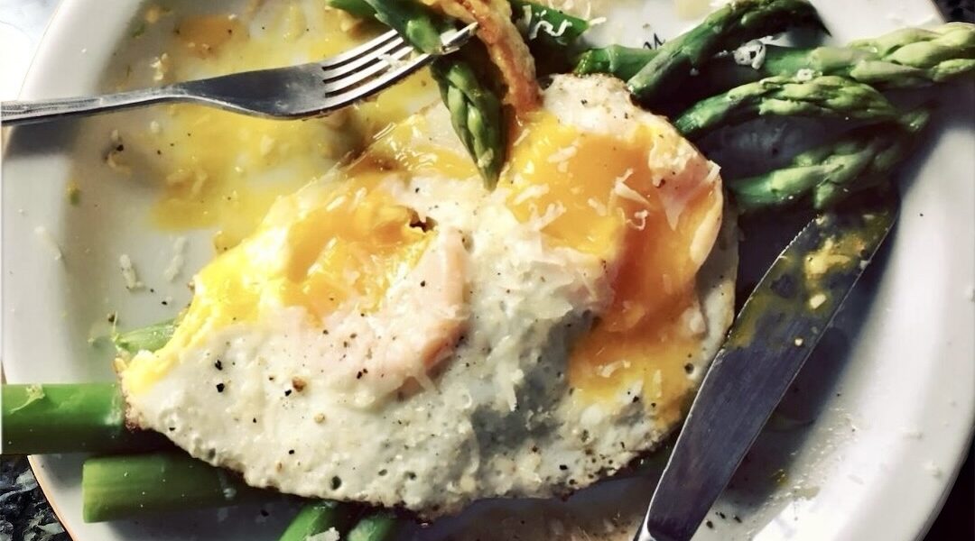 Krótko gotowane zielone szparagi podane z jajkiem sadzonym posypane świeżo startym serem parmezan.