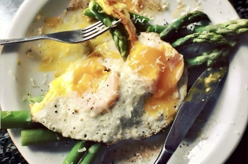 Krótko gotowane zielone szparagi podane z jajkiem sadzonym posypane świeżo startym serem parmezan.