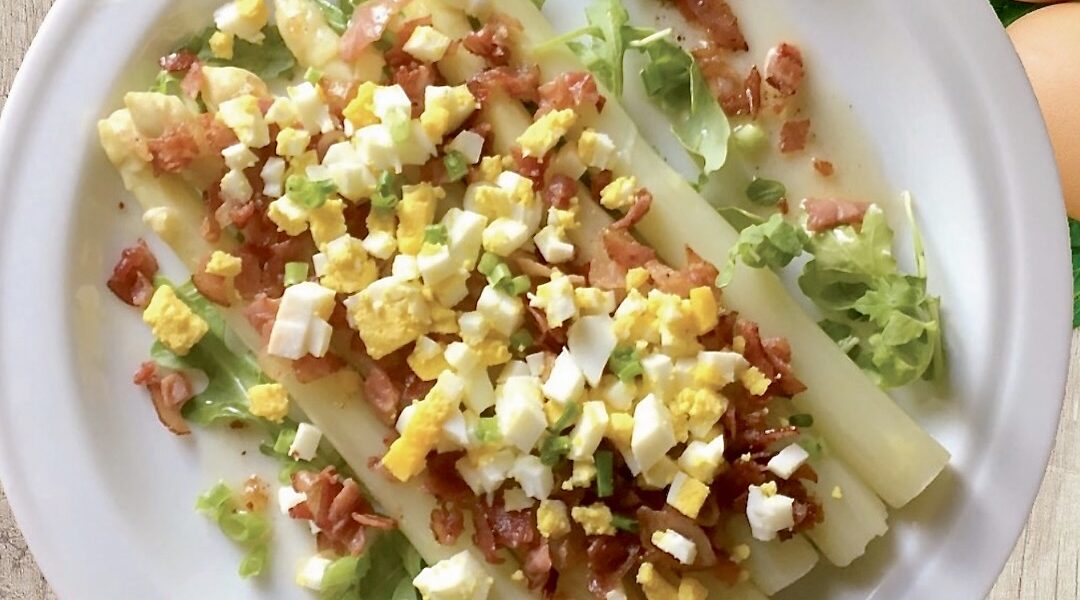 Ugotowane białe szparagi podane z przesmażoną szynką oraz startym gotowanym jajkiem.