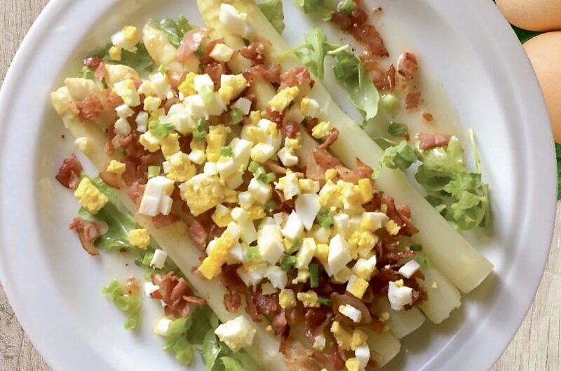 Ugotowane białe szparagi podane z przesmażoną szynką oraz startym gotowanym jajkiem.