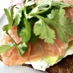 Tosty posmarowane serkiem i obłożone wędzonym łososiem z dodatkiem awokado i listkami kolendry.