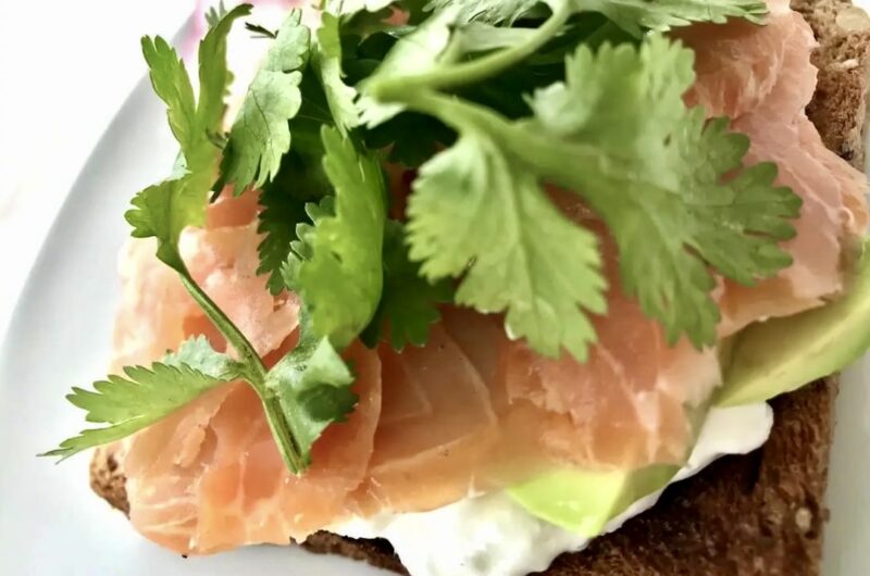 Tosty posmarowane serkiem i obłożone wędzonym łososiem z dodatkiem awokado i listkami kolendry.