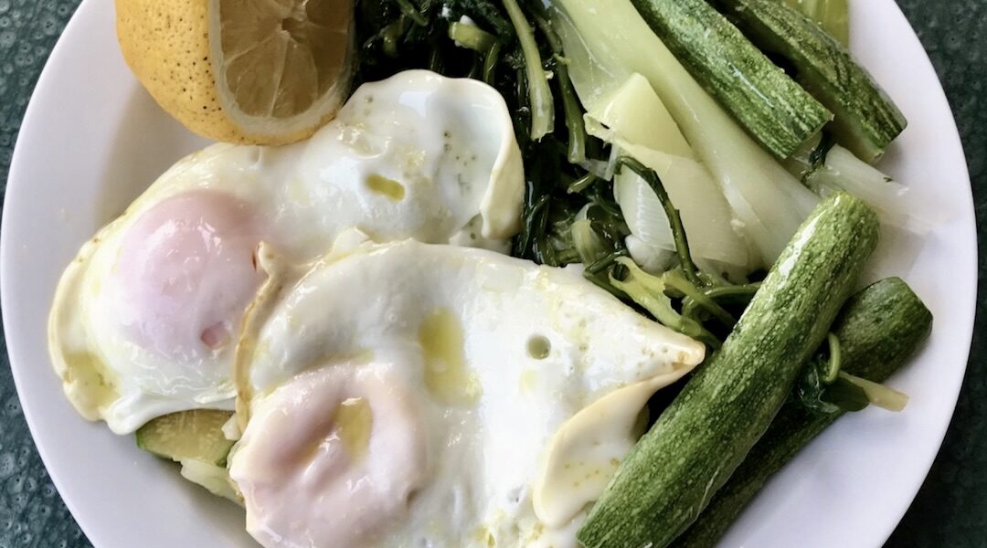 Gotowane warzywa czyli cykoria, cukinia i por podane z jajkiem sadzonym i w całości polane oliwą i sokiem z cytryny.