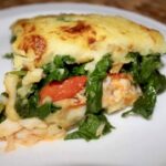 Zapiekanka z dorszem gotowanym bacalhao z puree ziemniaczanym, kiełbasą chorizo i liśćmi szpinaku.