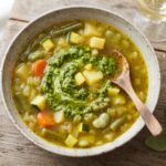 Zupa jarzynowa na bazie bulionu warzywnego z dodatkiem fasolki szparagowej, bobu i cukinii doprawiona domowym pesto bazyliowym.