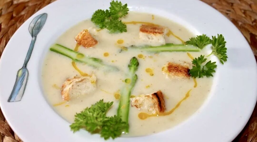 Zupa krem przygotowana z gotowanych białych szparagów doprawiona słodką śmietanką, a następnie zmiksowana i podana z zielonymi szparagami oraz grzankami.