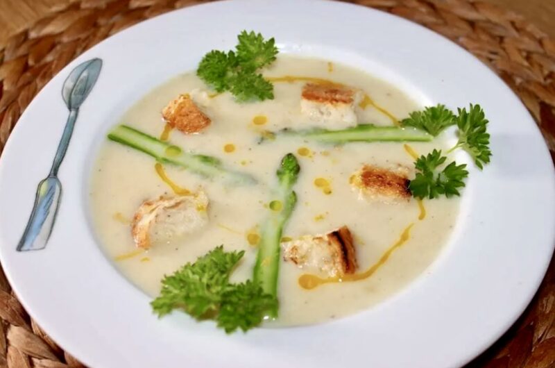 Zupa krem przygotowana z gotowanych białych szparagów doprawiona słodką śmietanką, a następnie zmiksowana i podana z zielonymi szparagami oraz grzankami.