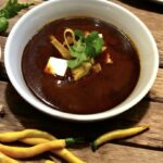 Zupa paprykowa przyrządzona z papryczek suszonych zmiksowanych z grillowanymi pomidorami i cebulą podana z tortillą pokrojoną w paski.