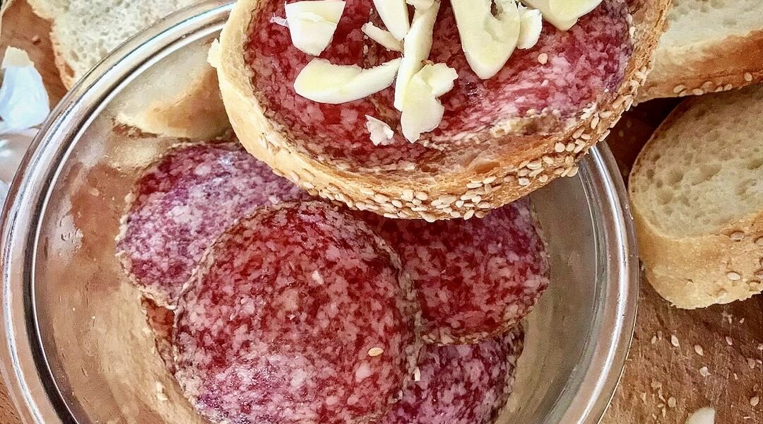 kromka białego pieczywa z plasterkami węgierskiego salami oraz z siekanym drobno czosnkiem