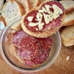 kromka białego pieczywa z plasterkami węgierskiego salami oraz z siekanym drobno czosnkiem