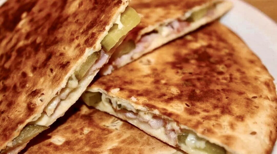 Quesadilla po góralsku czyli tortilla obłożona boczkiem, plasterkami ogórka kiszonego oraz ze startym oscypkiem, a następnie przykryta drugą tortilla i podgrzana na patelni.