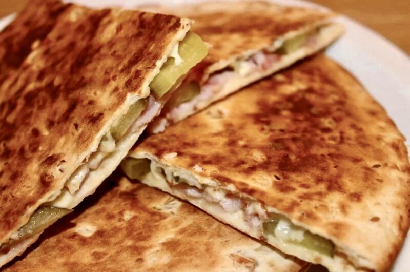 Quesadilla po góralsku czyli tortilla obłożona boczkiem, plasterkami ogórka kiszonego oraz ze startym oscypkiem, a następnie przykryta drugą tortilla i podgrzana na patelni.