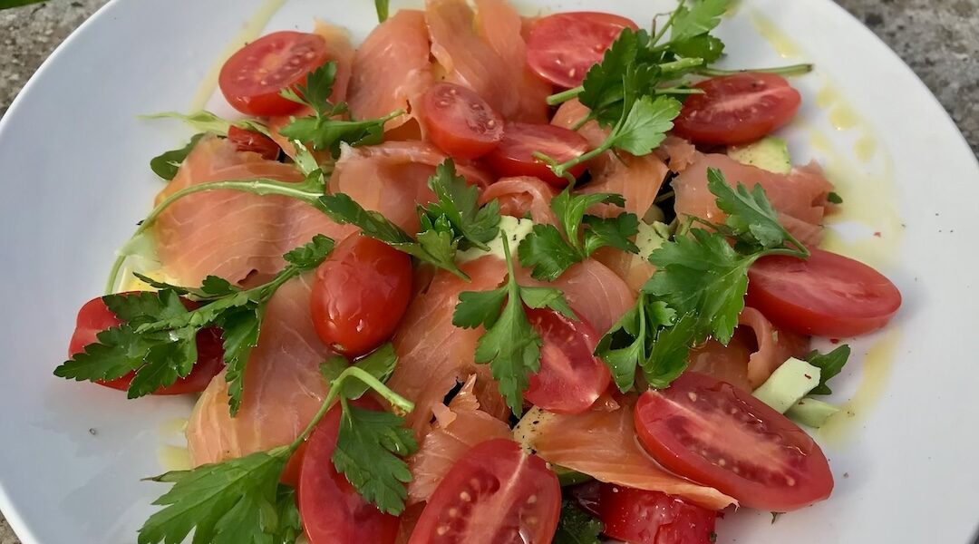 Sałatka łososiowa przygotowana z plasterków łososia wędzonego podanego z kawałkami awokado, z pomidorami koktajlowymi i czerwoną papryka. Sałatka przed podaniem skropiona została oliwą extra vergine i sokiem z cytryny.