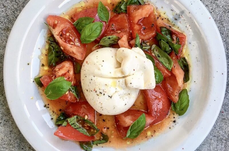 Burrata to unikatowy delikatny ser mozzarellą wypełniony śmietanką podany w tym przepisie razem z pomidorami koktajlowymi oliwa i świeżą bazylią.