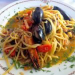 Makaron ugotowany al dente podany na dużym talerzu w sosie z oliwą i owocami morza.