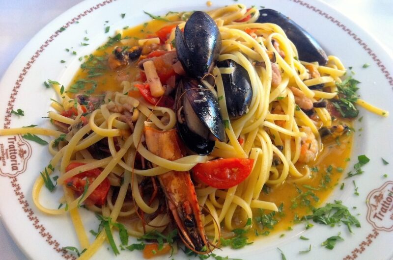 Makaron ugotowany al dente podany na dużym talerzu w sosie z oliwą i owocami morza.