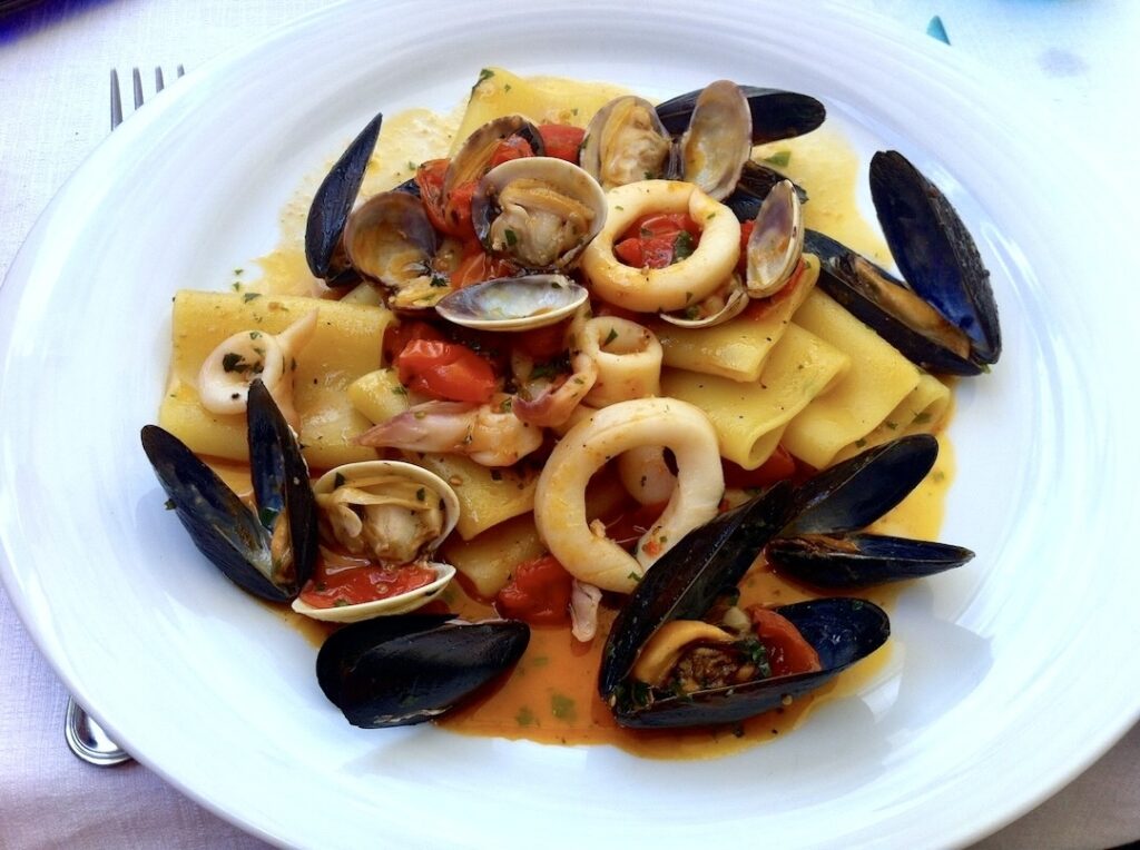 Makaron ugotowany al dente podany na białym talerzu z sosem z oliwy, pomidorów i owoców morza