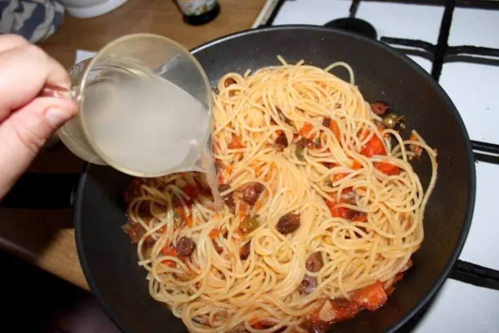 Woda z gotowania makaronu dolewana do makaronu z sosem znajdujących się na dużej patelni