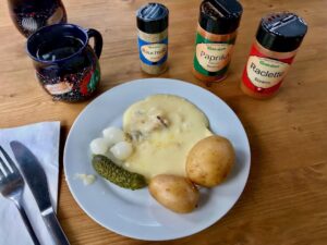 talerz ze stopionym serem raclette oraz gotowanymi ziemniakami i kiszonym ogórkiem