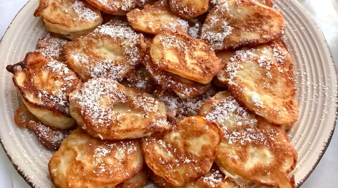 Racuchy z jabłkami, czyli małe placki przygotowane z plasterków jabłek otoczonych ciastem naleśnikowym, usmażone na złoto, posypane cukrem pudrem.