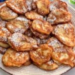 Racuchy z jabłkami, czyli małe placki przygotowane z plasterków jabłek otoczonych ciastem naleśnikowym, usmażone na złoto, posypane cukrem pudrem.