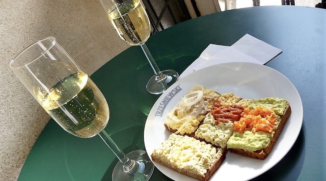 na zielonym stole znajduje się biały talerzyk z kanapkami, a obok stoją dwa kieliszki z szampanem