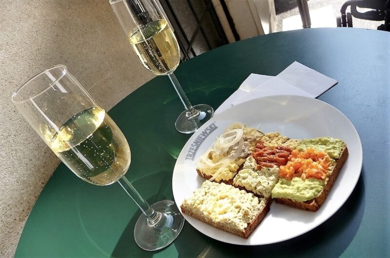 na zielonym stole znajduje się biały talerzyk z kanapkami, a obok stoją dwa kieliszki z szampanem