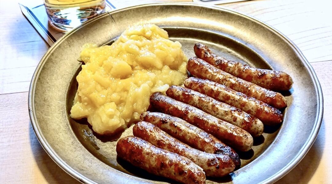 Małe smażone kiełbaski wieprzowe na talerzu w towarzystwie puree ziemniaczanego.