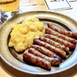 Małe smażone kiełbaski wieprzowe na talerzu w towarzystwie puree ziemniaczanego.