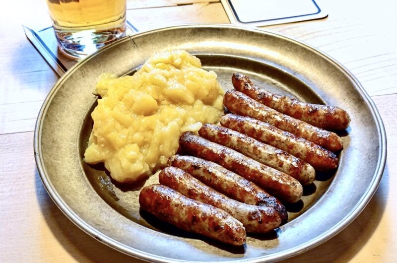 Małe smażone kiełbaski wieprzowe na talerzu w towarzystwie puree ziemniaczanego.