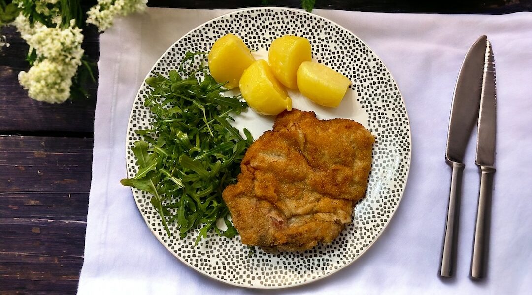 Kotlet cielęcy z kością delikatnie roztłuczony na cienko, panierowany w tradycyjny sposób w jajku i bułce tartej, a następnie smażony na tłuszczu.