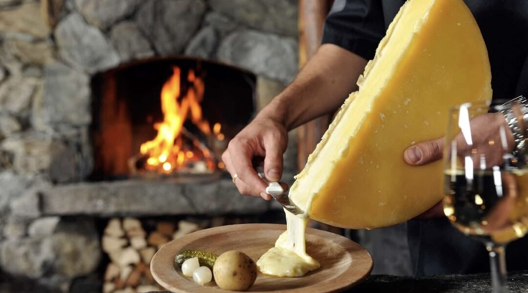 mężczyzna skrobie z gomółki nożem na talerz stopiony ser raclette