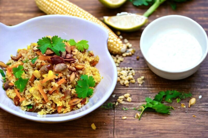 Sałatka z komosą ryżową z dodatkiem marchewki, świeżej kolendry, gotowanej kukurydzy ora pestek dyni w białej misce na drewnianym blacie