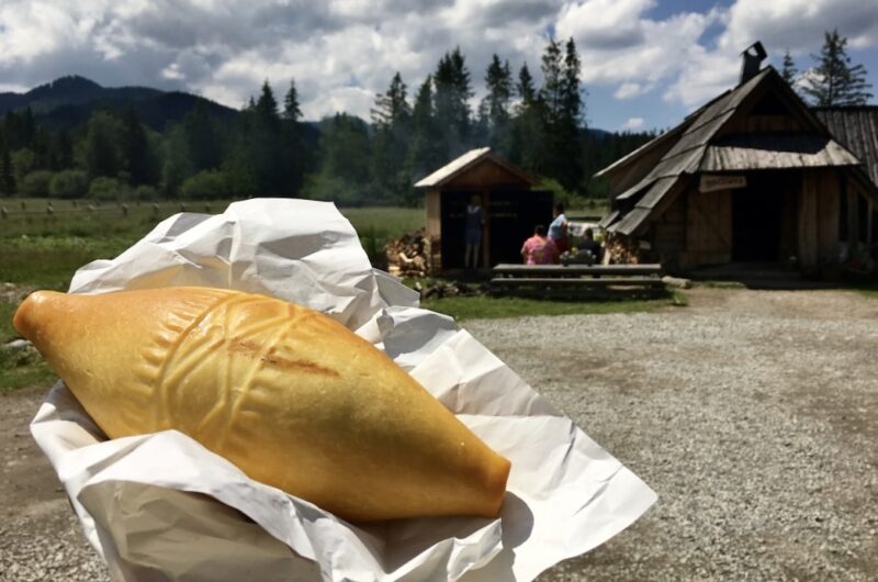 świeżo wędzony oscypek na papierze trzymany w dłoni z bacówką w tle