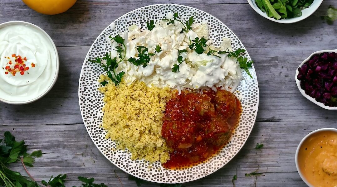 Surówka z kapusty pekińskiej z sosem czosnkowym podana na talerzu z pulpetami w sosie pomidorowym oraz z kuskusem