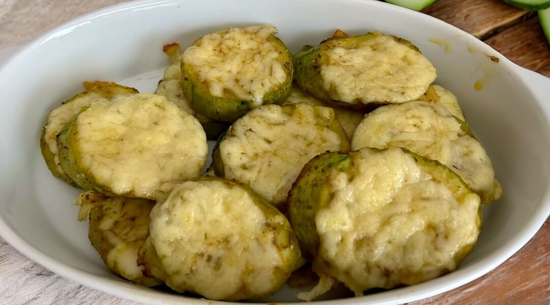 cukinia pokrojona w plastry, obłożona startym serem i czosnkiem, a następnie krótko zapiekana