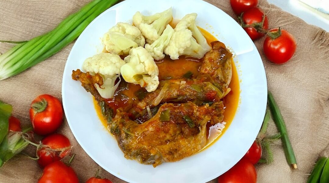 na talerzu znajduje się królik duszony w sosie pomidorowym razem z zieloną dymką oraz różyczki ugotowanego kalafiora