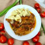 na talerzu znajduje się królik duszony w sosie pomidorowym razem z zieloną dymką oraz różyczki ugotowanego kalafiora