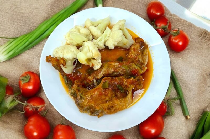 na talerzu znajduje się królik duszony w sosie pomidorowym razem z zieloną dymką oraz różyczki ugotowanego kalafiora