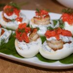 Ugotowane i przekrojone wzdłuż na połowę jajka obłożone dipem koperkowym oraz usmażonymi krewetkami.