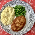 kotlet pożarski na talerzu razem z puree z ziemniaków oraz gotowanym zielonym groszkiem