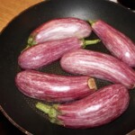 na patelni smażą się przekrojone wzdłuż na pół bakłażany