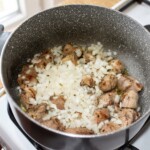 w duży garnku smaży się siekana cebula razem mięsem krojonym w sporą kostkę