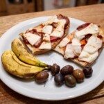 grzanki z szynką i serem z Krety podane na talerzu z oliwkami i lokalnymi bananami