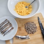 w misce znajdują się ugniecione ugotowane żółtka kurze, obok są siekane drobno fileciki anchois
