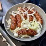 na patelni smażą się laseczki kiełbasy śląskiej razem z celu pokrojoną w piórka