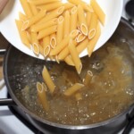 makaron penne wrzucany jest do garnka z gotująca się wodą